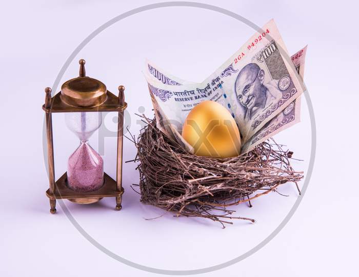 hourglass with Golden egg and indian money or paper currency notes in a real nest. Shallow focus.