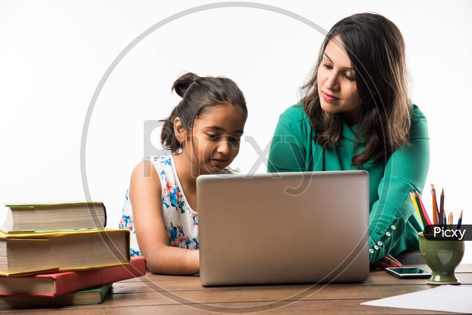 Indian girl studying with mother at study table with laptop and books