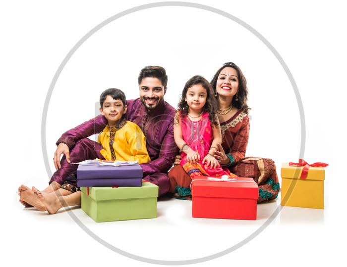 Indian family celebrating Diwali / Deepavali in traditional wear while sitting isolated over white background with gift boxes an