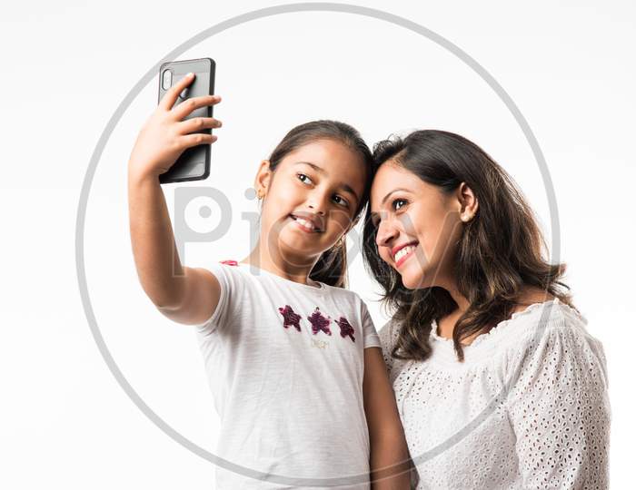 Indian/asian mother daughter taking selfie picture with smartphone, isolated over white background