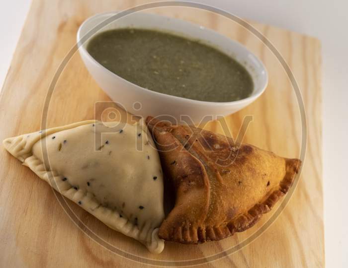 Uncooked and cooked Indian Samosa on a wooden plate with coriander  chilli sauce (chatni).
