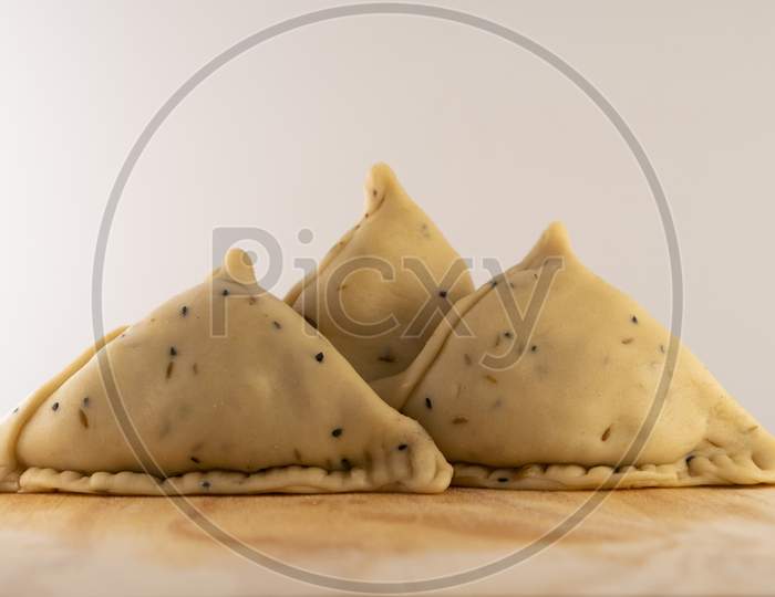 Uncooked samosa on a wooden plate .