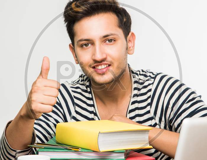 Young male college student studying on study table with books and laptop at home or classroom