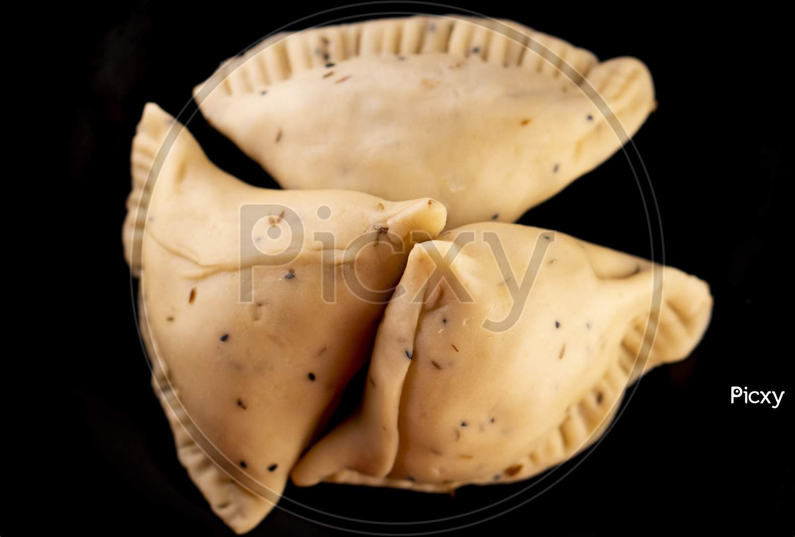 Uncooked samosa on a black plate .