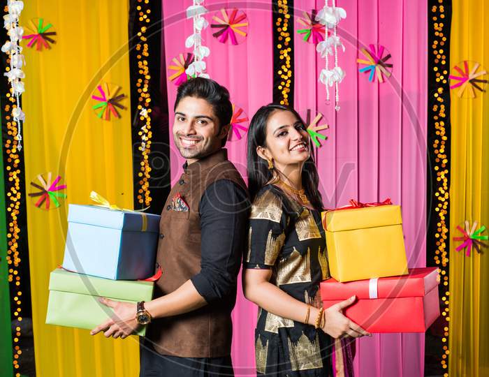 Smart Indian couple standing with gift boxes on Diwali festival or wedding ceremony