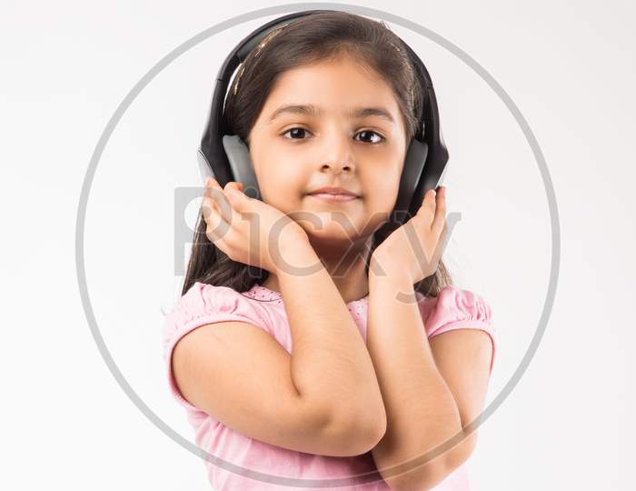 Cute Indian/asian small girl listening to music on wireless headphones isolated on white