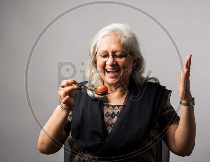 Senior Indian/asian lady eating sweet Gulab Jamun with spoon