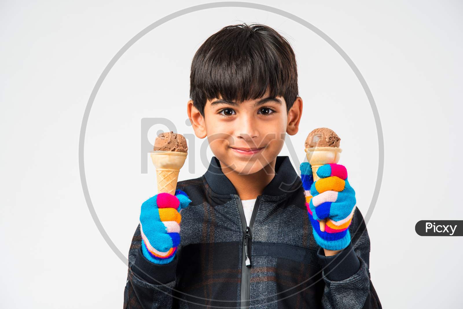 Indian kid / boy eating ice cream in warm clothes on white background