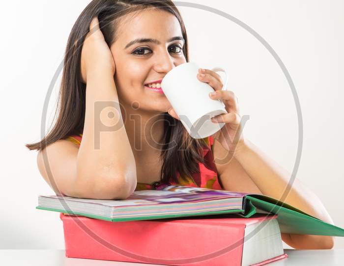 Pretty Indian/Asian collage Girl studying on tablet with pile of books