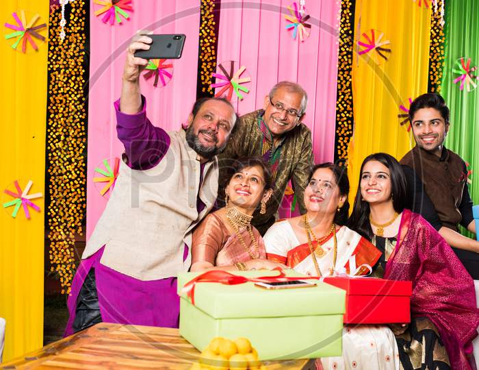 Indian family taking selfie picture using smartphone while wearing traditional festival cloths on diwali/wedding ceremony and si