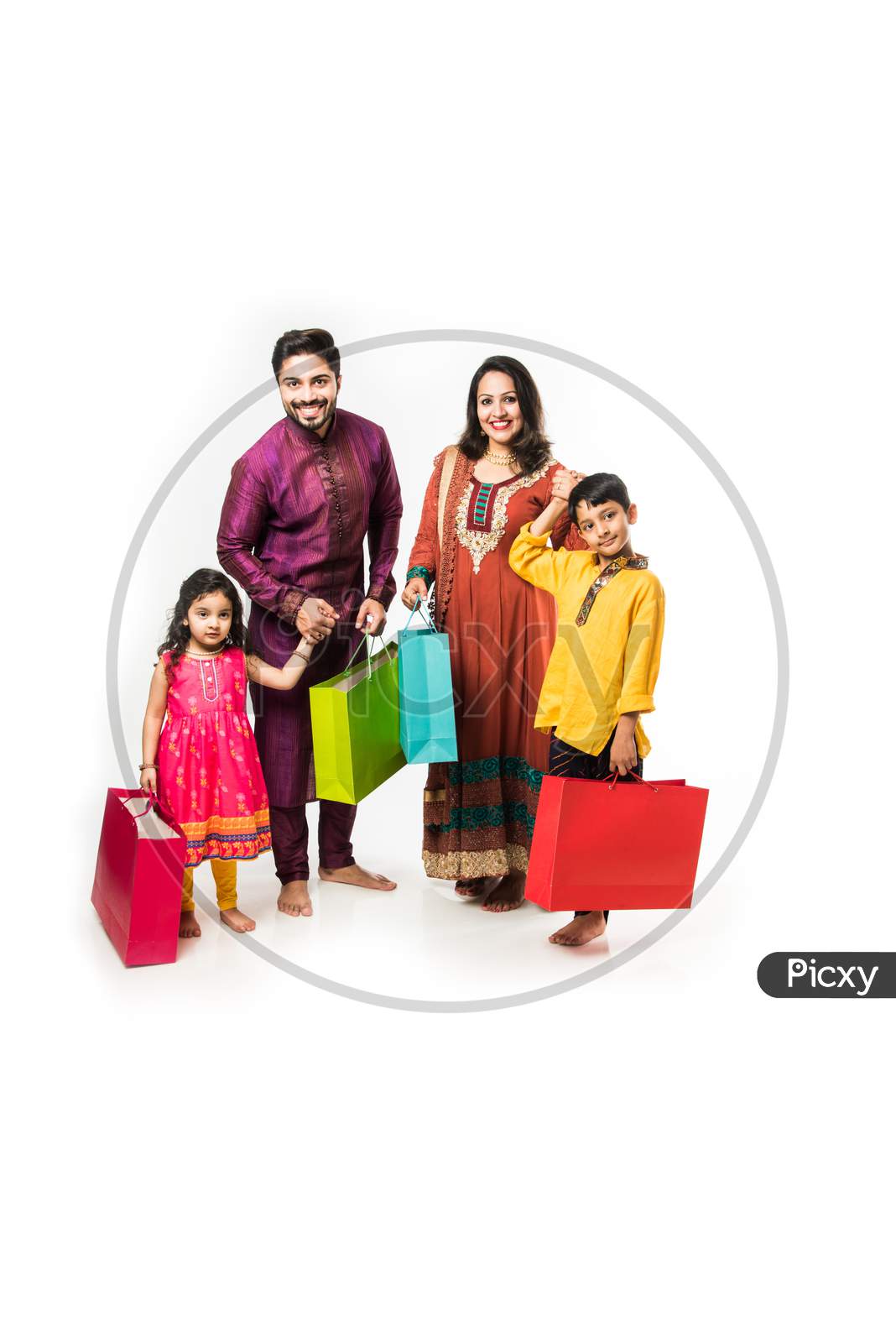 Indian family celebrating Diwali / Deepavali in traditional wear with shopping bags, standing isolated over white background