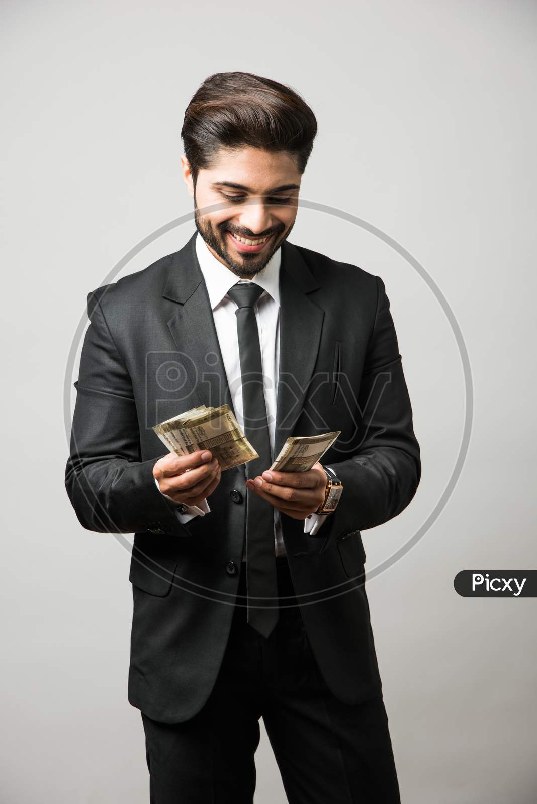 Happy bearded Indian businessman holding fan in hand, Indian Rupee currency bills of 500 , standing isolated over white backgrou