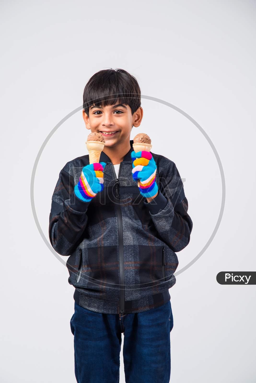 Indian kid / boy eating ice cream in warm clothes on white background