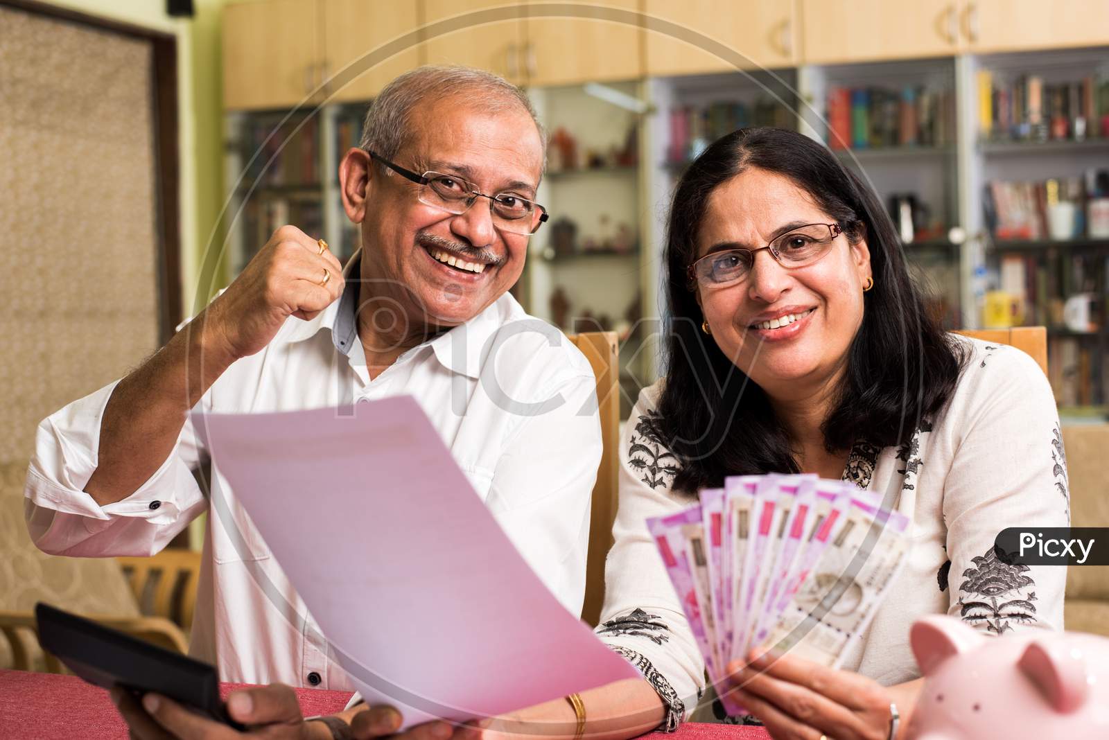 Senior Indian/asian couple accounting, doing home finance and checking bills with laptop, calculator and money while sitting on