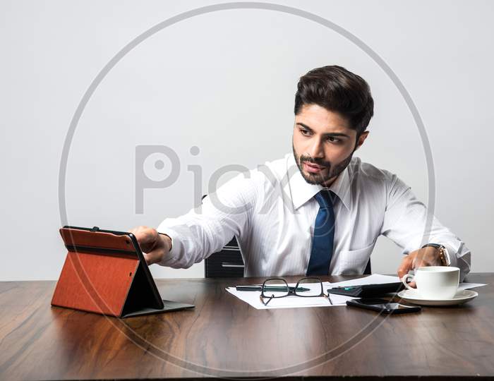 Bearded Indian Businessman accounting while sitting at desk / table in office