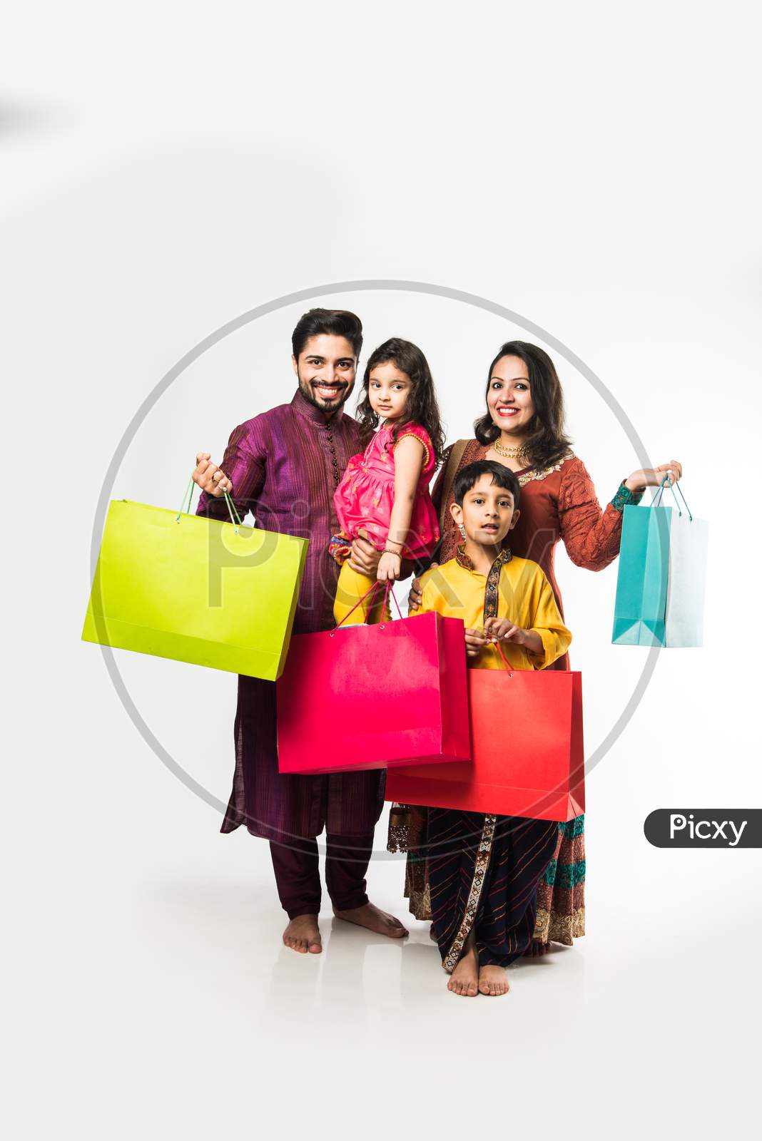 Indian family celebrating Diwali / Deepavali in traditional wear with shopping bags, standing isolated over white background