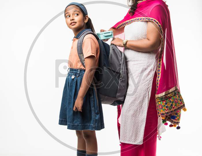 Indian Mother helping school girl with uniform getting ready with Lunch Box, hair style or waiting for school bus