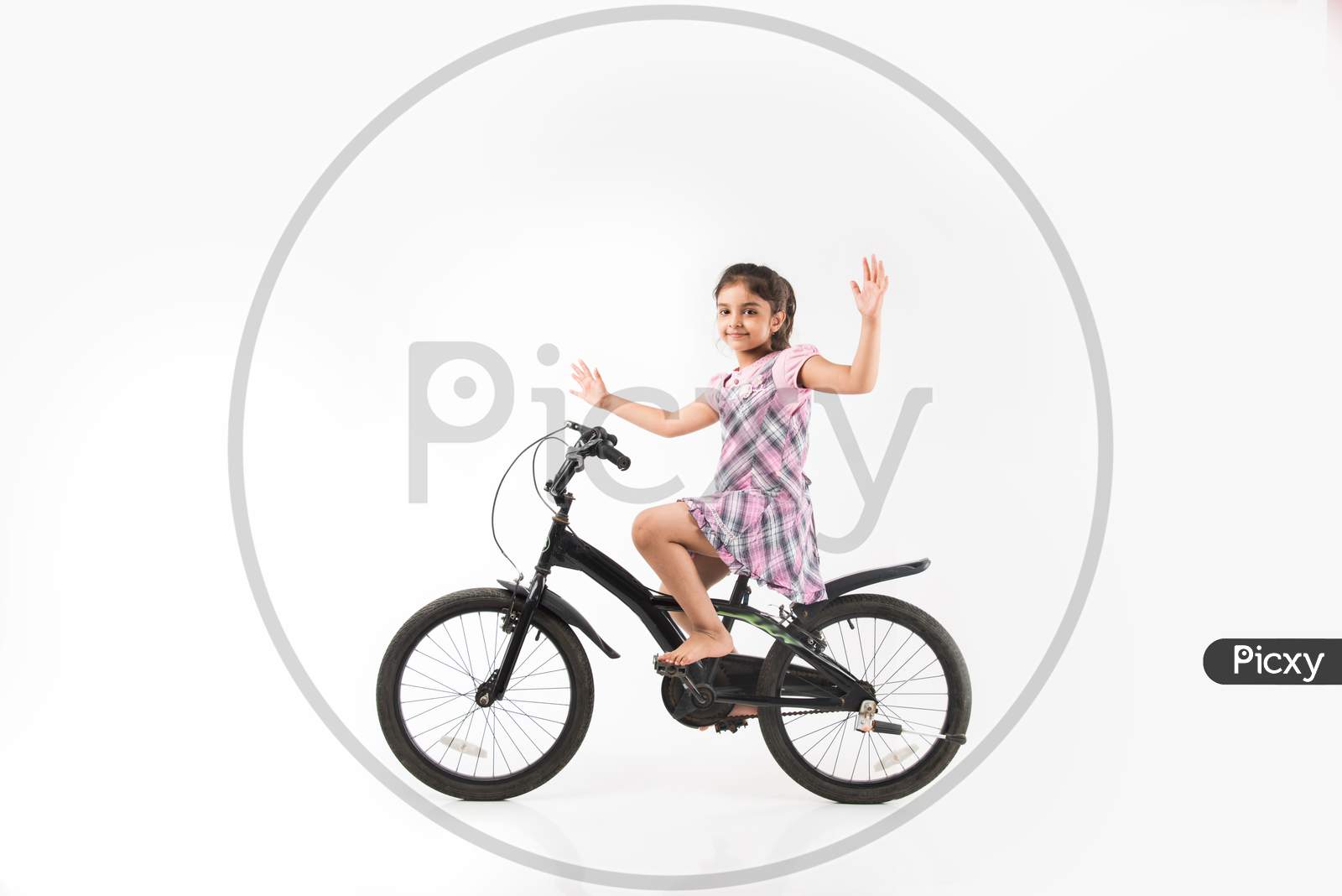 Cute little Indian/asian girl riding on bicycle, isolated over white background