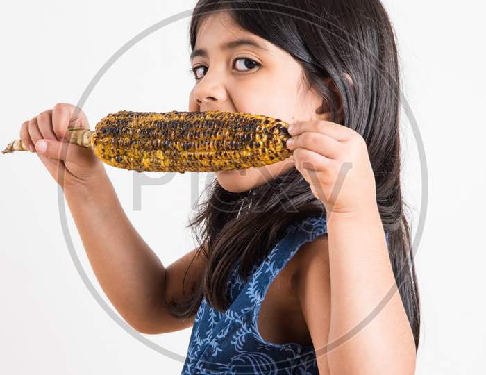 Cute little indian girl eating Grilled Corn or Bhutta, Standing isolated over white background