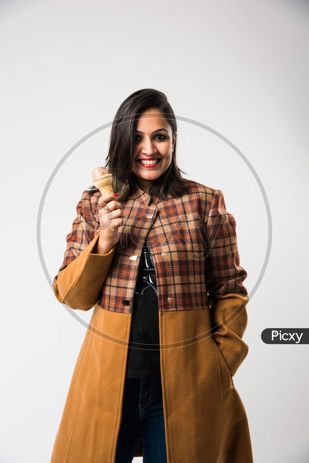 Indian girl / female eating ice cream while wearing warm winter clothes on white background
