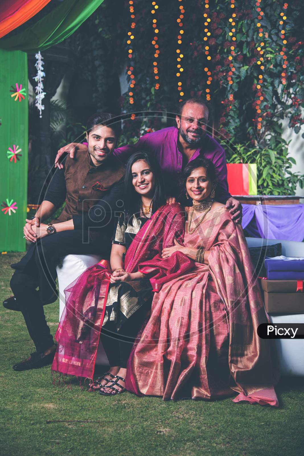 Indian Family posing for group photo on festival or wedding night, sitting on couch or round table with background decorated wit