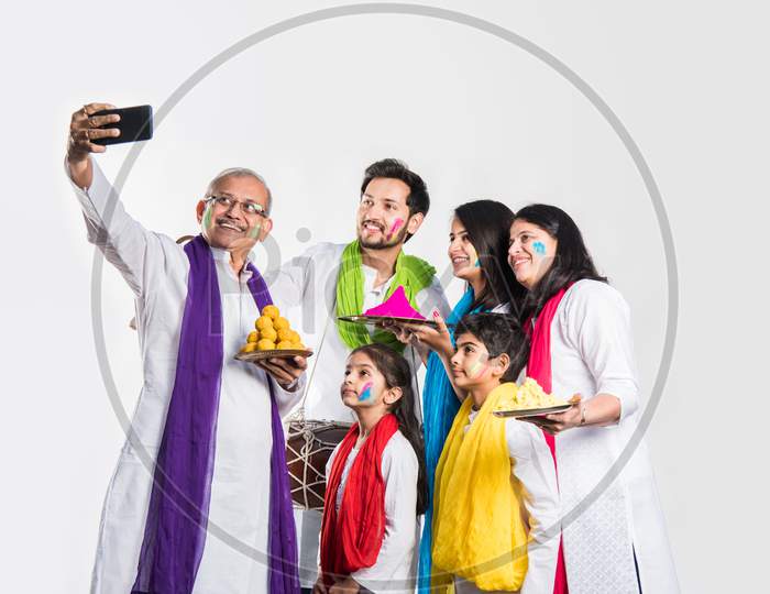 Indian Family taking selfie picture on Holi festival while holding sweets and colours