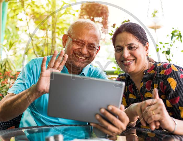 Indian/asian Senior couple video chatting on tablet/computer while sitting at couch or in garden at home, selective focus