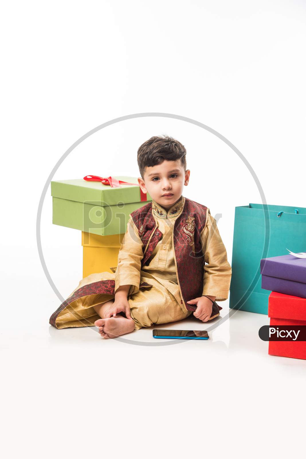 Portrait of Cute little Indian boy in traditional wear using smartphone / mobile playing games or watching videos, isolated over