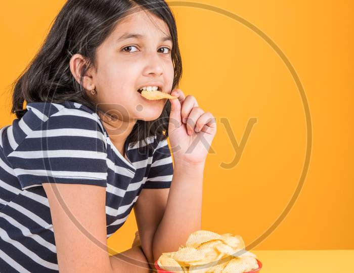 Cute little girl eating potato wafers or crispy chips