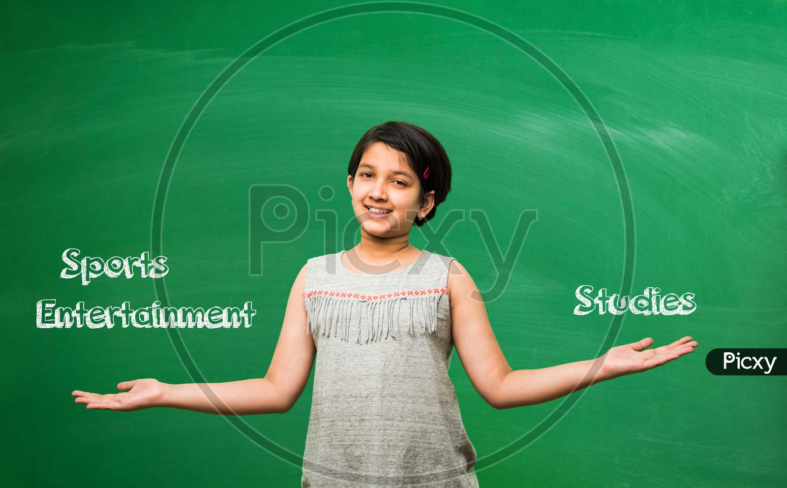 Little school girl standing in front of green scalk board with doodles - education and kids concept