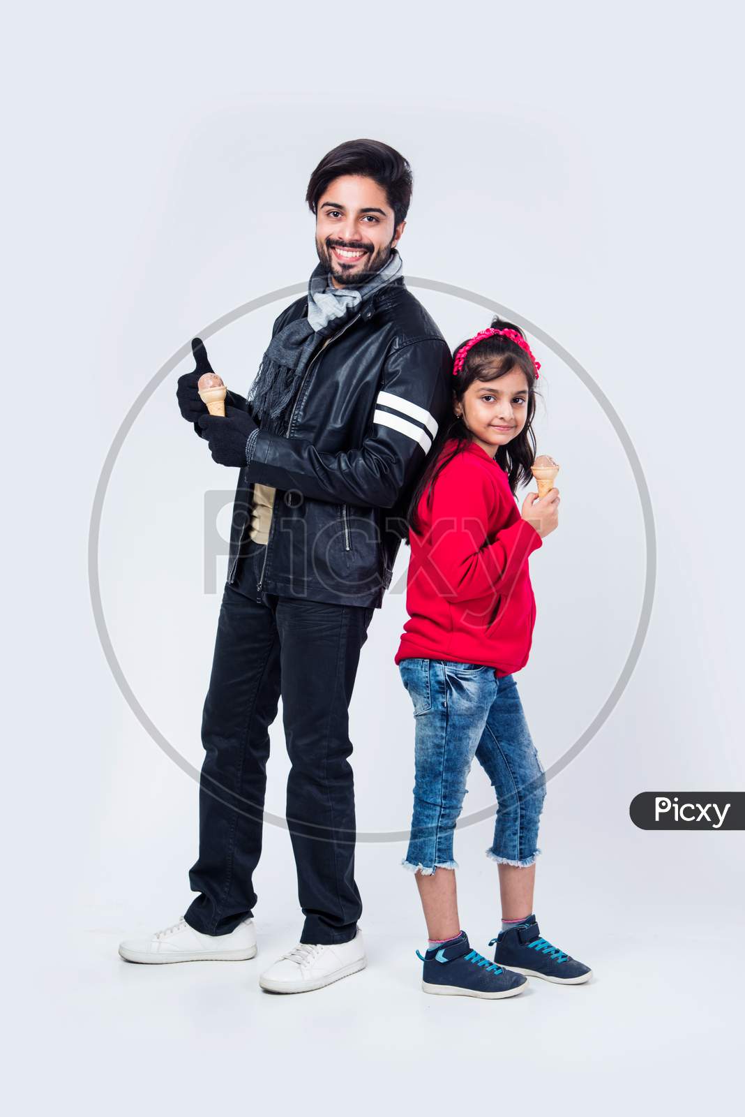Indian father and daughter eating ice cream in cone while wearing warm clothes on white background