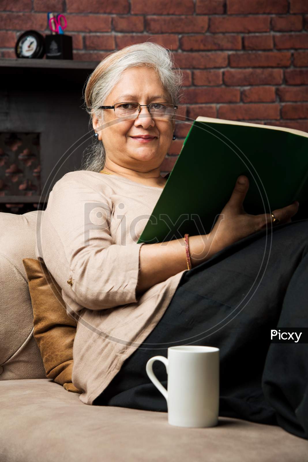 cute Senior indian/asian lady sitting on recliners chair or sofa reading book or using tab or laptop computer