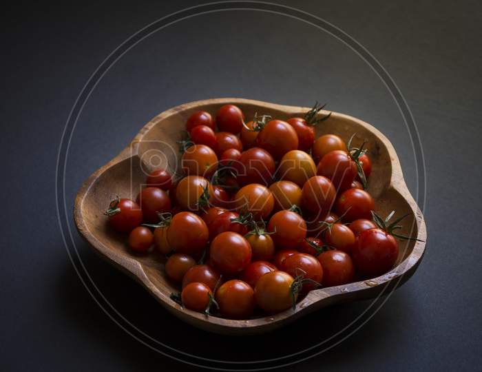 A wooden bowl full of red fresh cherry or baby tomatoes.
