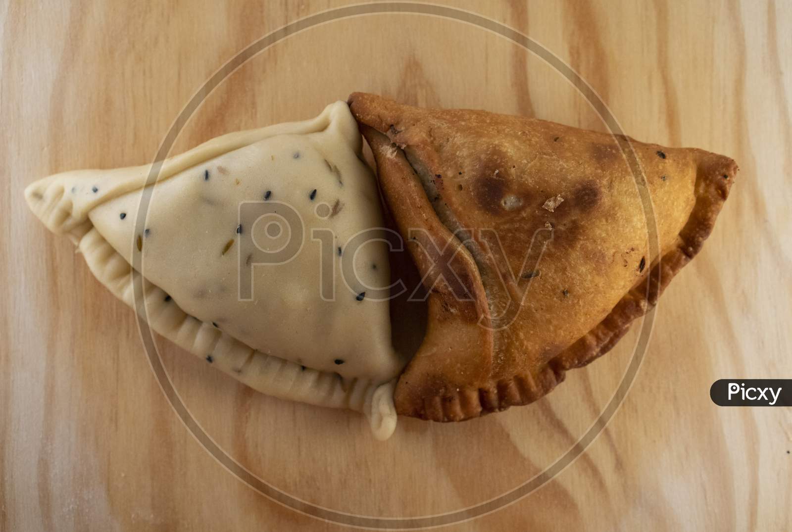 Uncooked and cooked Indian Samosa on a wooden plate .