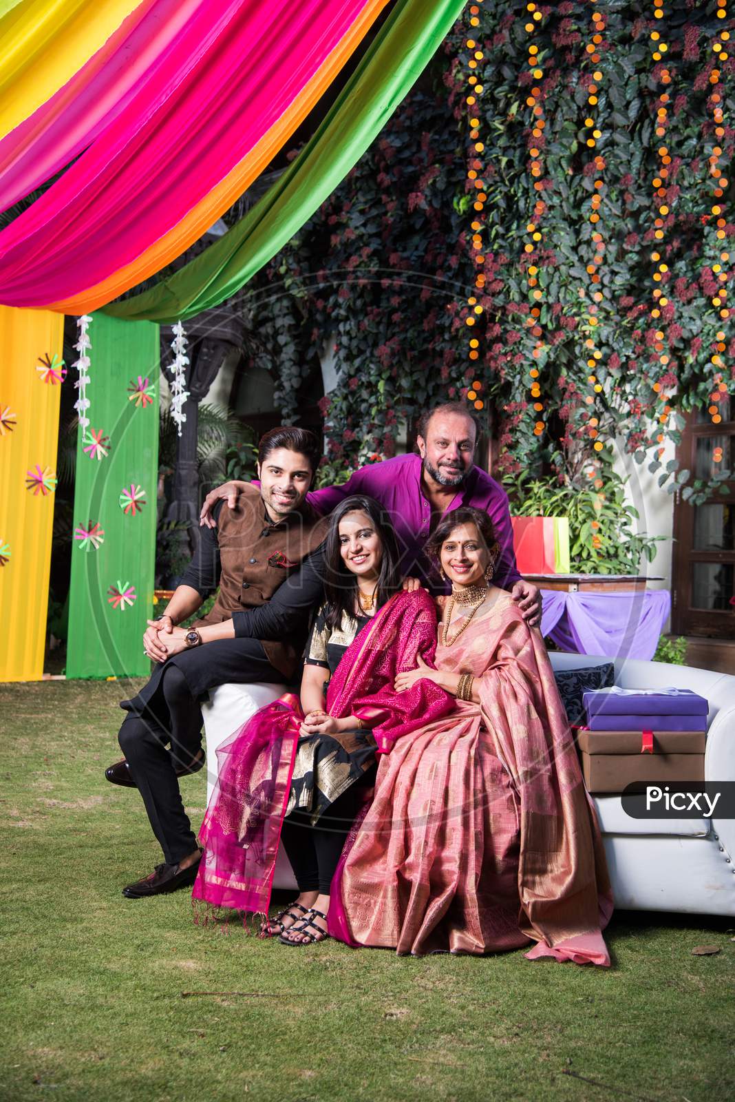 Indian Family posing for group photo on festival or wedding night, sitting on couch or round table with background decorated wit