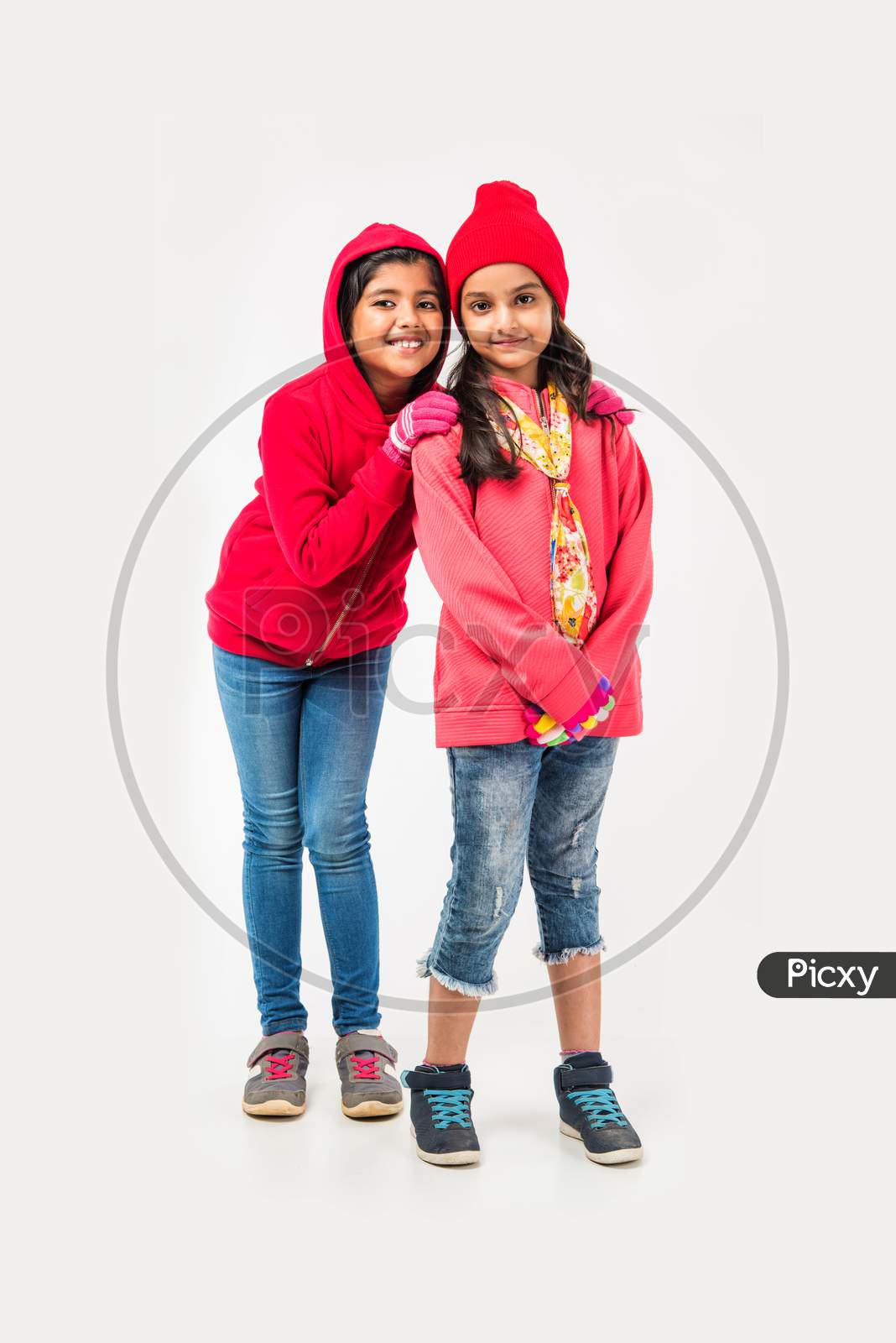 Two Indian cute little girls in winter wear, standing against white background