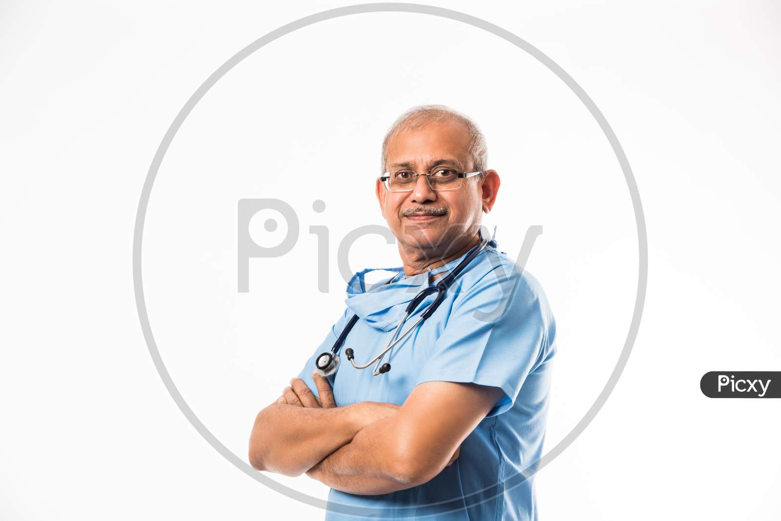 Senior Indian male surgeon in blue dress, standing with stethoscope over white background