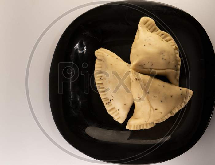 Uncooked samosa on a black plate .