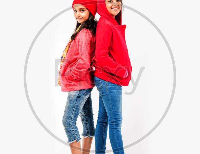 Two Indian cute little girls in winter wear, standing against white background