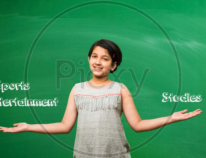 Little school girl standing in front of green scalk board with doodles - education and kids concept