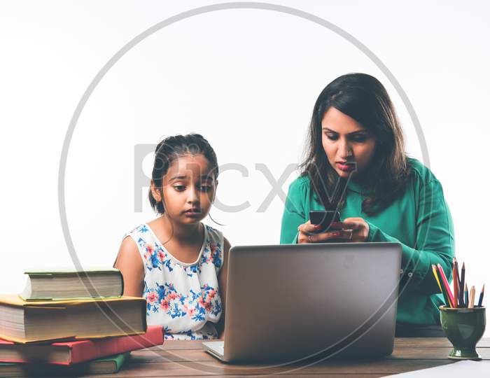 Indian girl studying with mother at study table with laptop and books