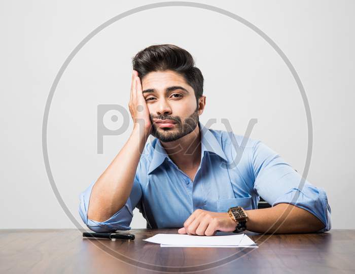 Stressed Indian Businessman having headache or Migraine pain while working at office table