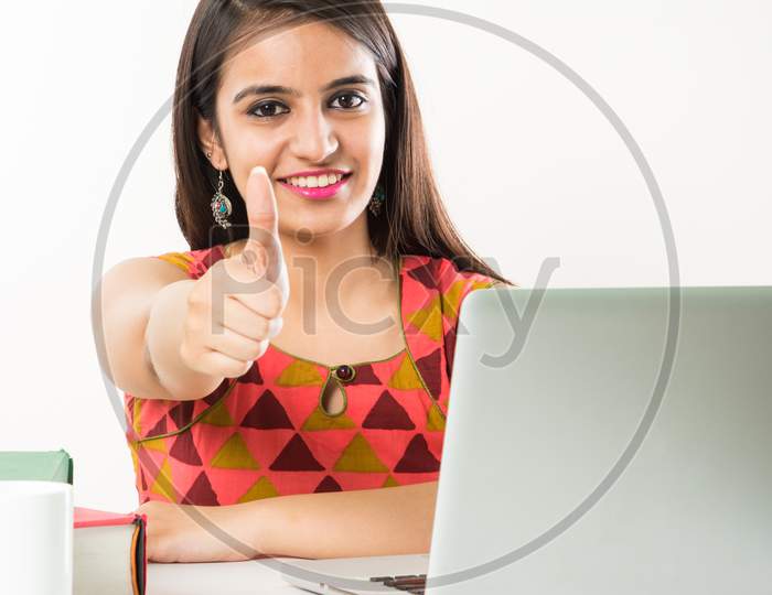 Pretty Indian/Asian Girl studying on laptop computer with pile of books on table, over white background
