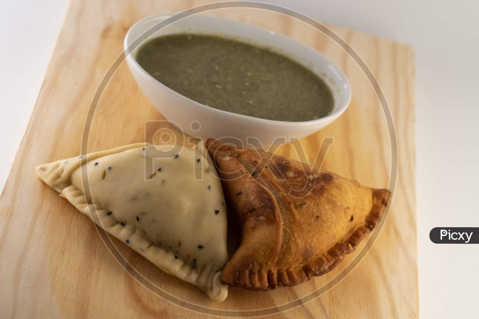 Uncooked and cooked Indian Samosa on a wooden plate with coriander  chilli sauce (chatni).
