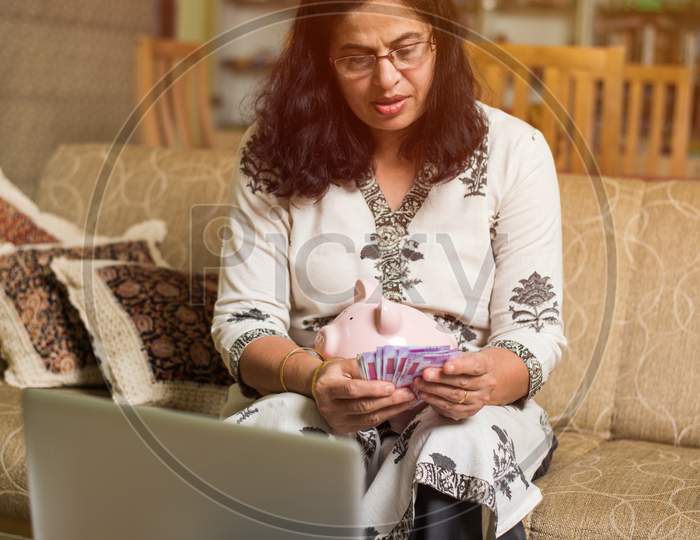Senior Indian/asian lady/women accounting with cash and laptop at home, selective focus