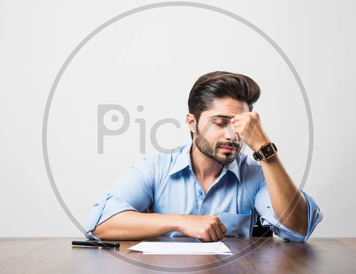 Stressed Indian Businessman having headache or Migraine pain while working at office table