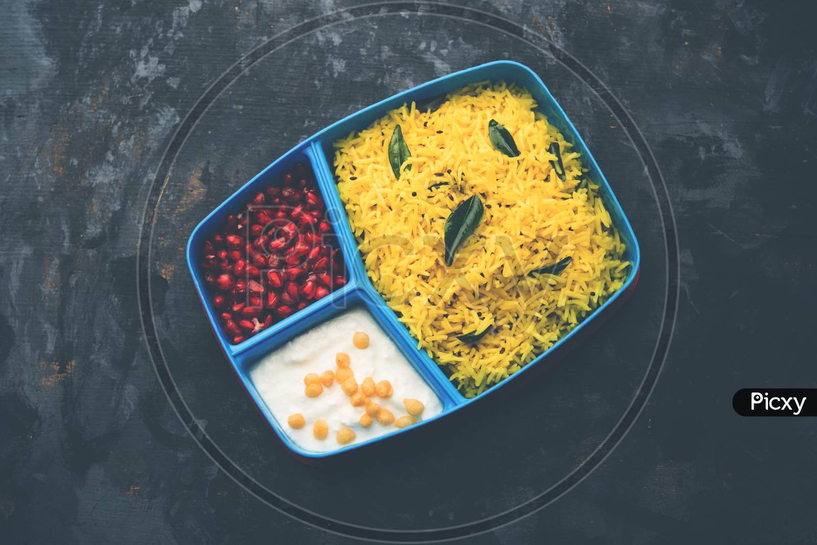 Lunch Box / Tiffin for Indian kids, contains lemon rice, nahi-boondi and pomegranate or Anar. selective focus
