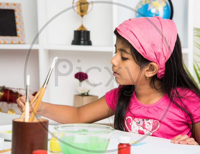 Cute Little Indian/Asian girl child enjoying drawing OR painting with brush and paint over paper at home