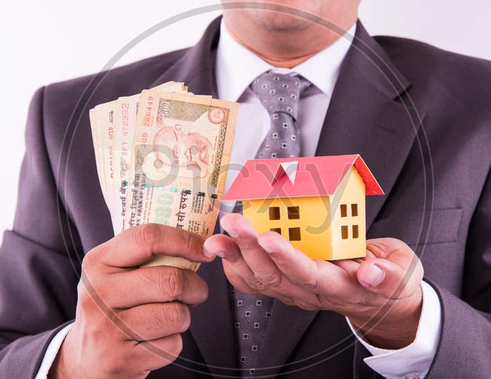 Home buying or real estate in India - Closeup of indian man holding indian Rupees and 3D home model