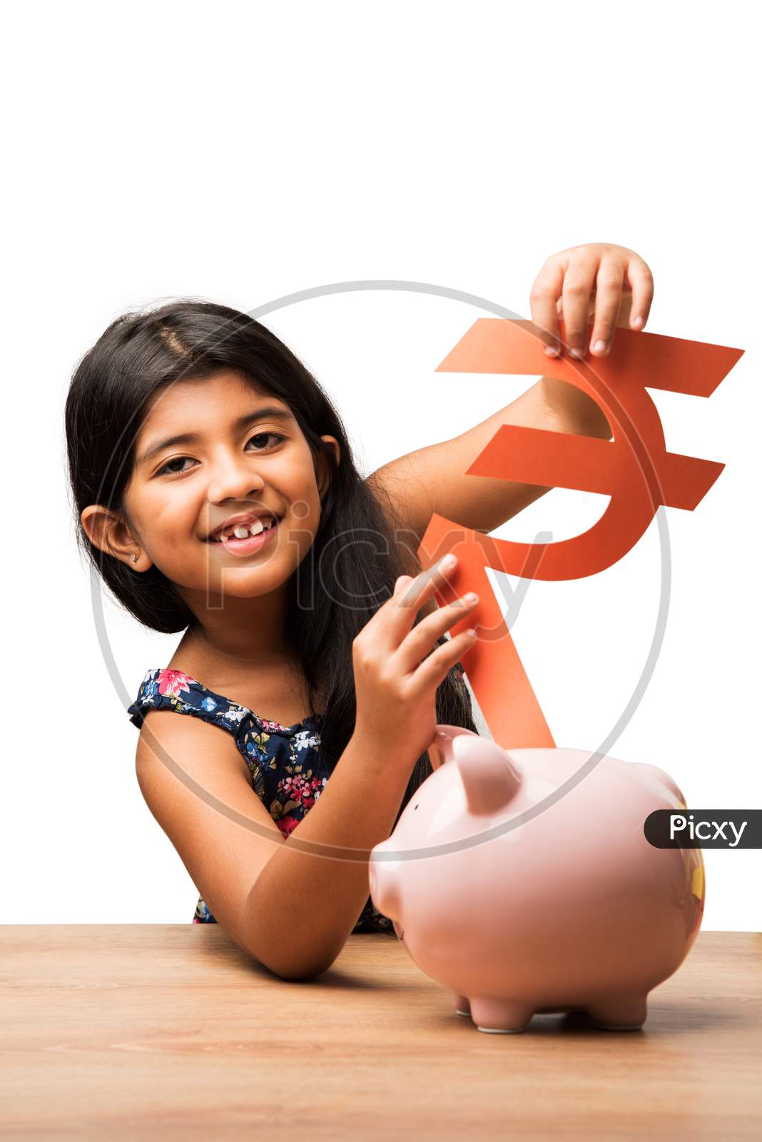 Small Girl inserting Paper Rupee symbol in piggybank
